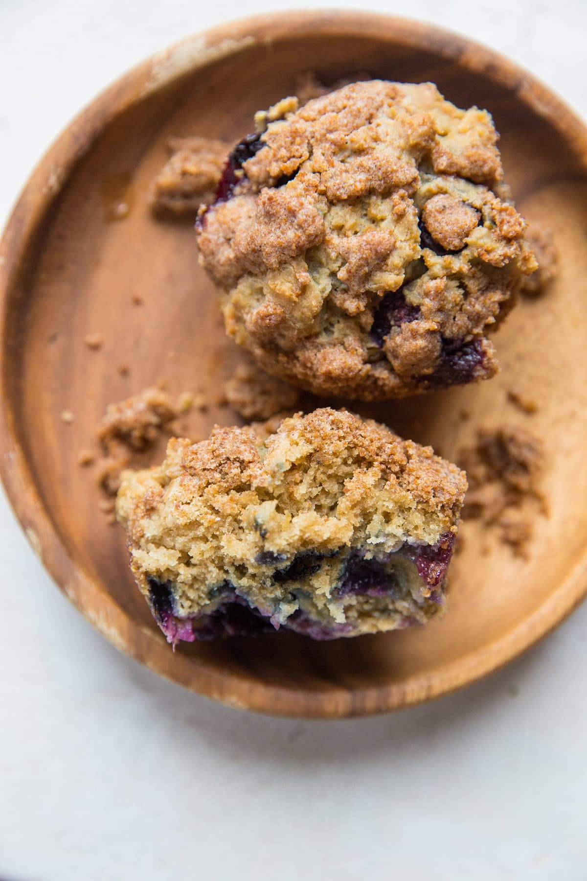 One wooden plate with two blueberry muffins with bite taken out of one.