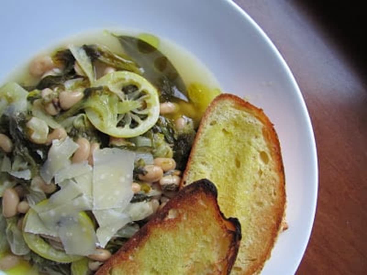 Braised Escarole & Beans in a large bowl with toasted buttered bread to the side and parmesan shavings.