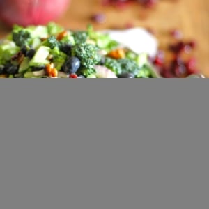 Broccoli salad in a bowl with dried cranberries to the side and forks to the side.