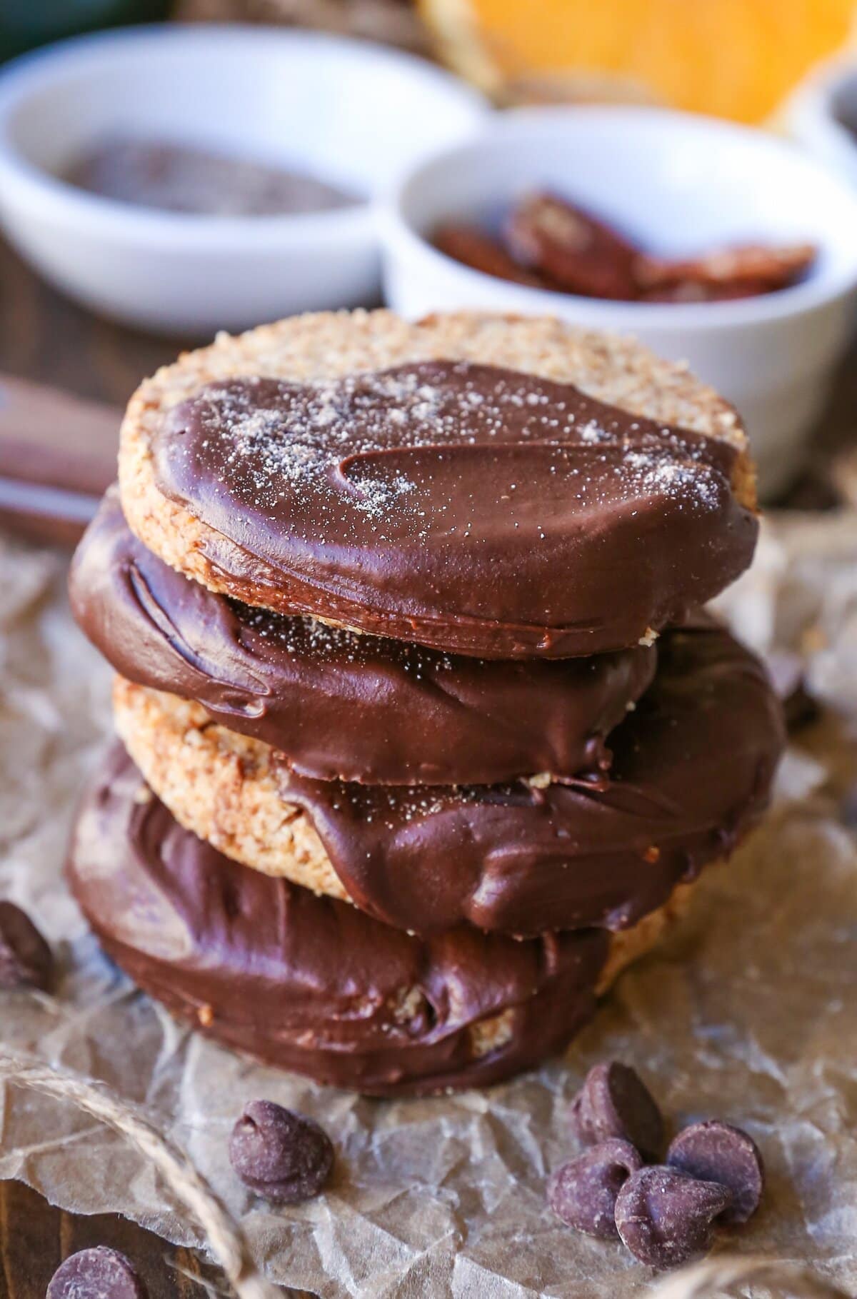 Stack of chocolate dipped shortbread cookies with nuts, chocolate chips and an orange in the background.