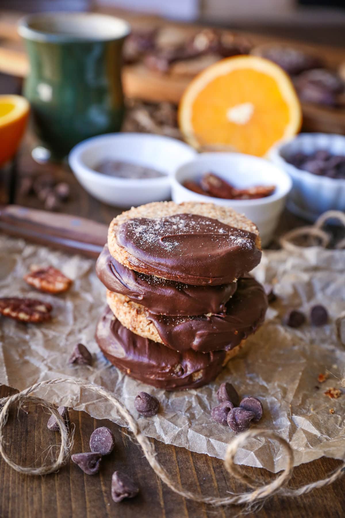 Four cardamom orange cookies stacked on top of each other with nuts and chocolate in the background.