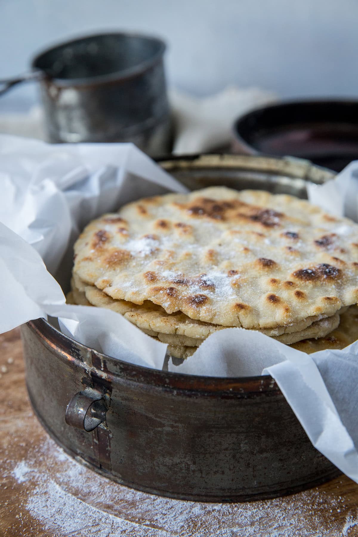 Basket of cassava flour tortillas lined in parchment paper on a wood cutting board with flour around the cutting board.
