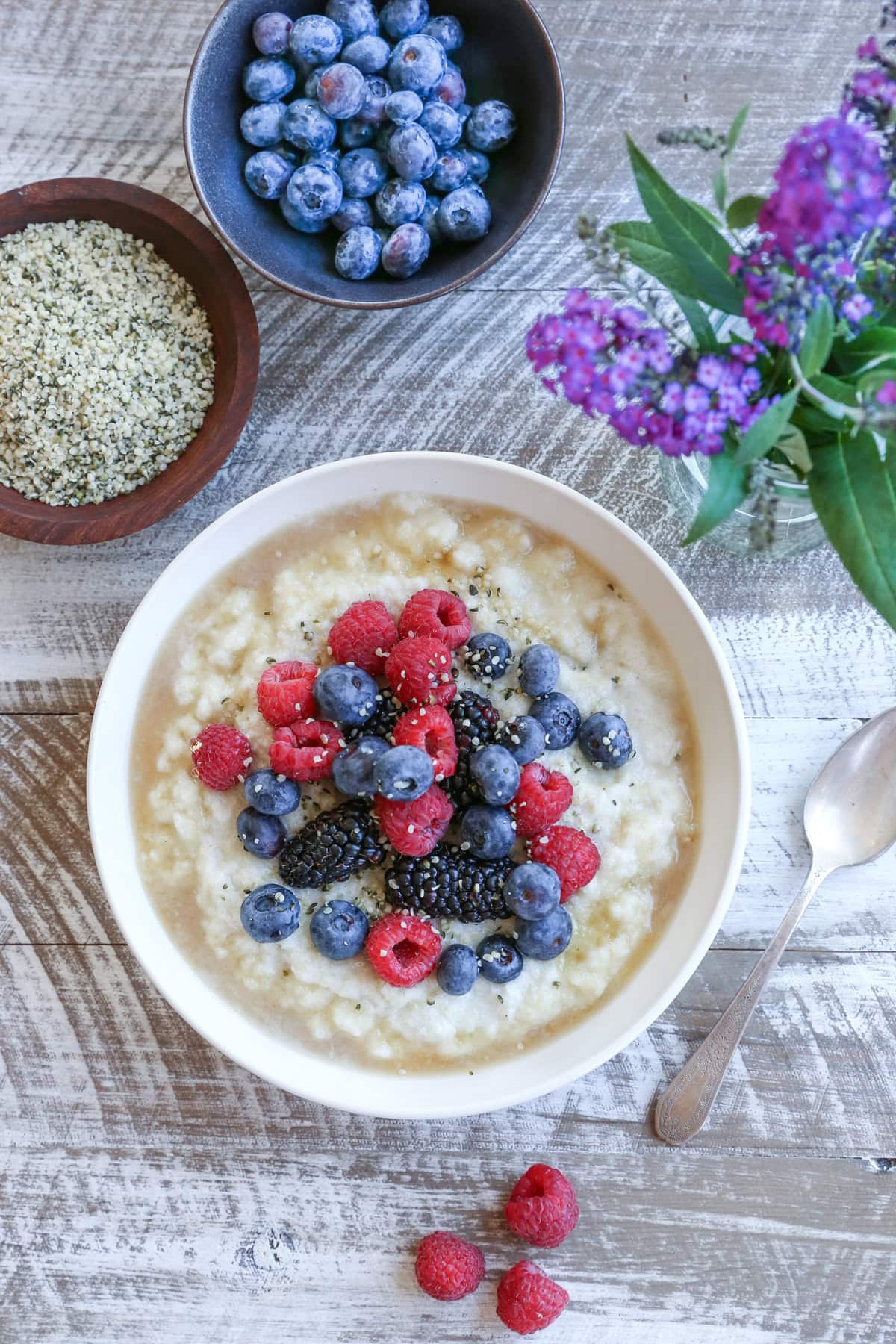 Bowl of cauliflower rice porridge on a white rustic table with berries to the side.
