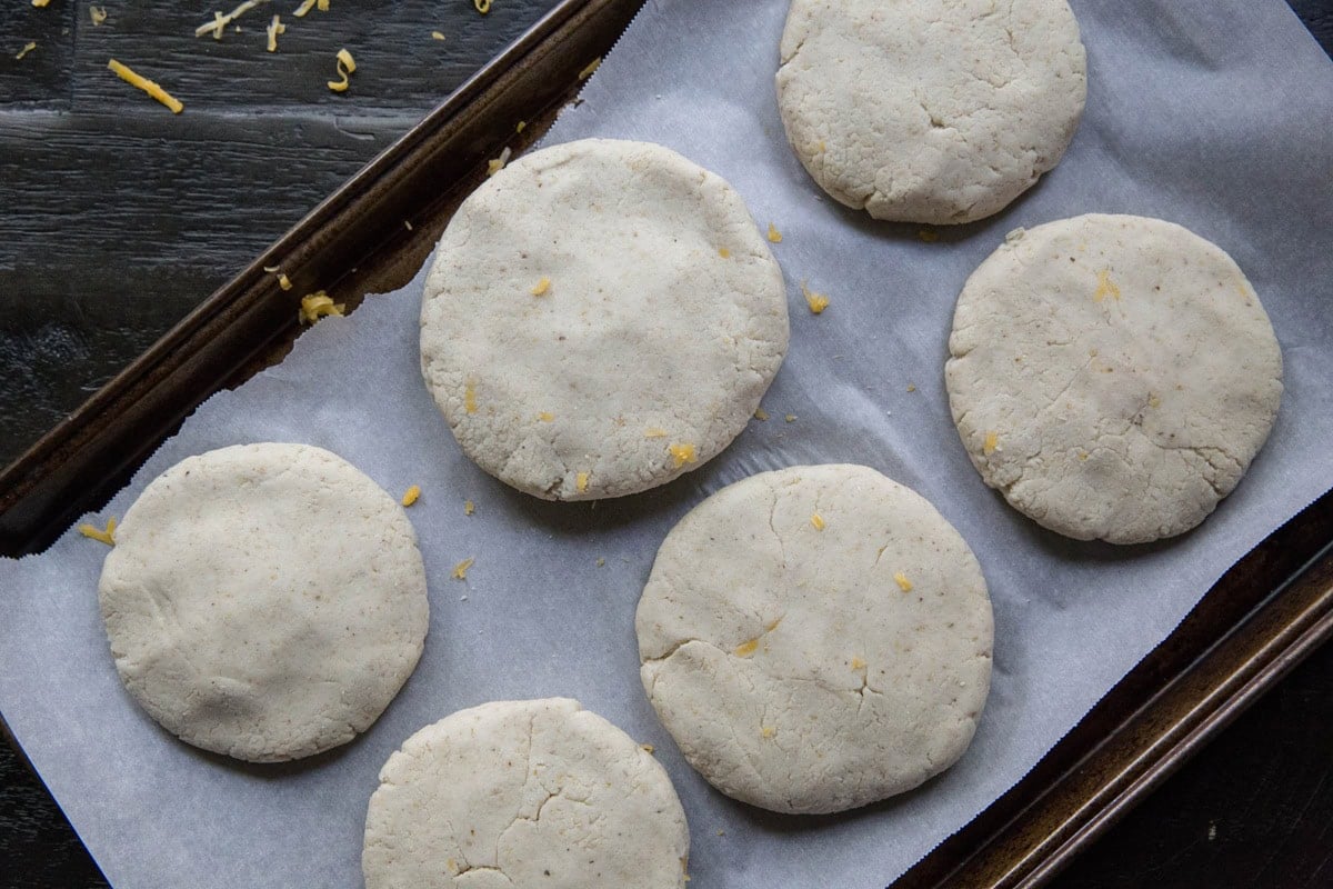 Raw prepared pupusas on a baking sheet, ready to be pan-fried.