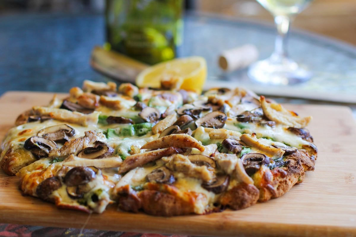 Pesto chicken pizza cut into slices on a cutting board.