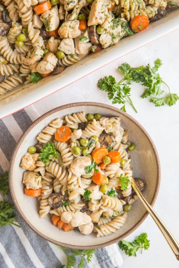 Creamy Chicken Noodle Casserole in a bowl with a golden spoon and a napkin with fresh parsley to the side.