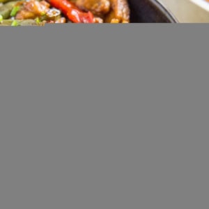 Large blue bowl full of chicken teriyaki on top of white rice, sprinkled with green onions and sesame seeds. Chopsticks and a napkin to the side.