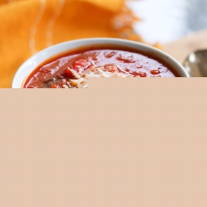 White bowl of tomato soup with a napkin and a spoon, ready to eat.
