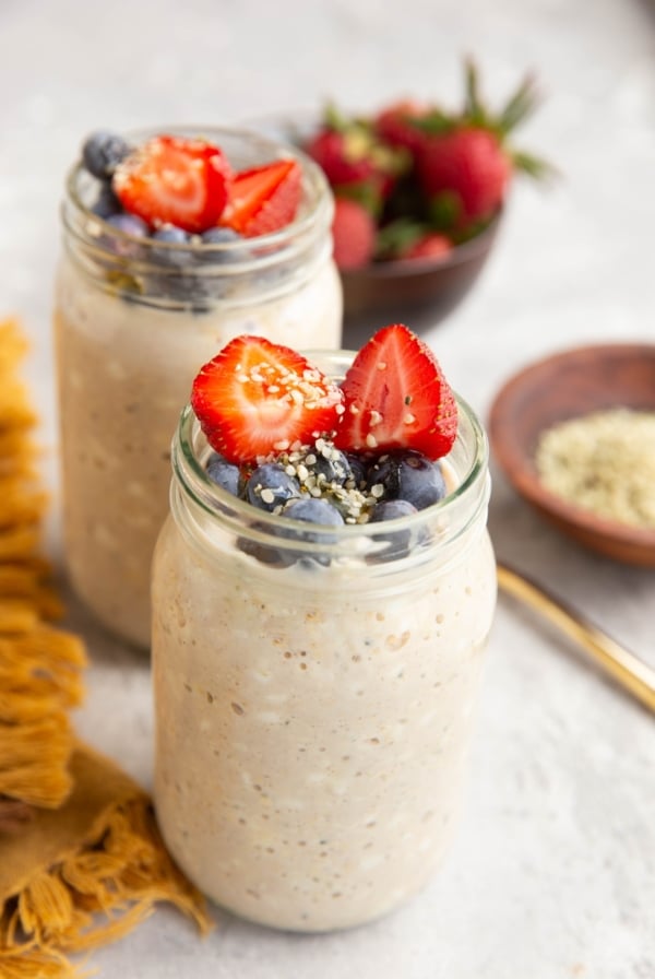 Two jars full of cottage cheese overnight oats with fresh fruit on top and a bowl of strawberries in the background.