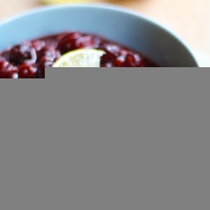 Cranberry Sauce with Ginger and Maple recipe inside of a blue bowl sitting on top of a pretty napkin and a cutting board.