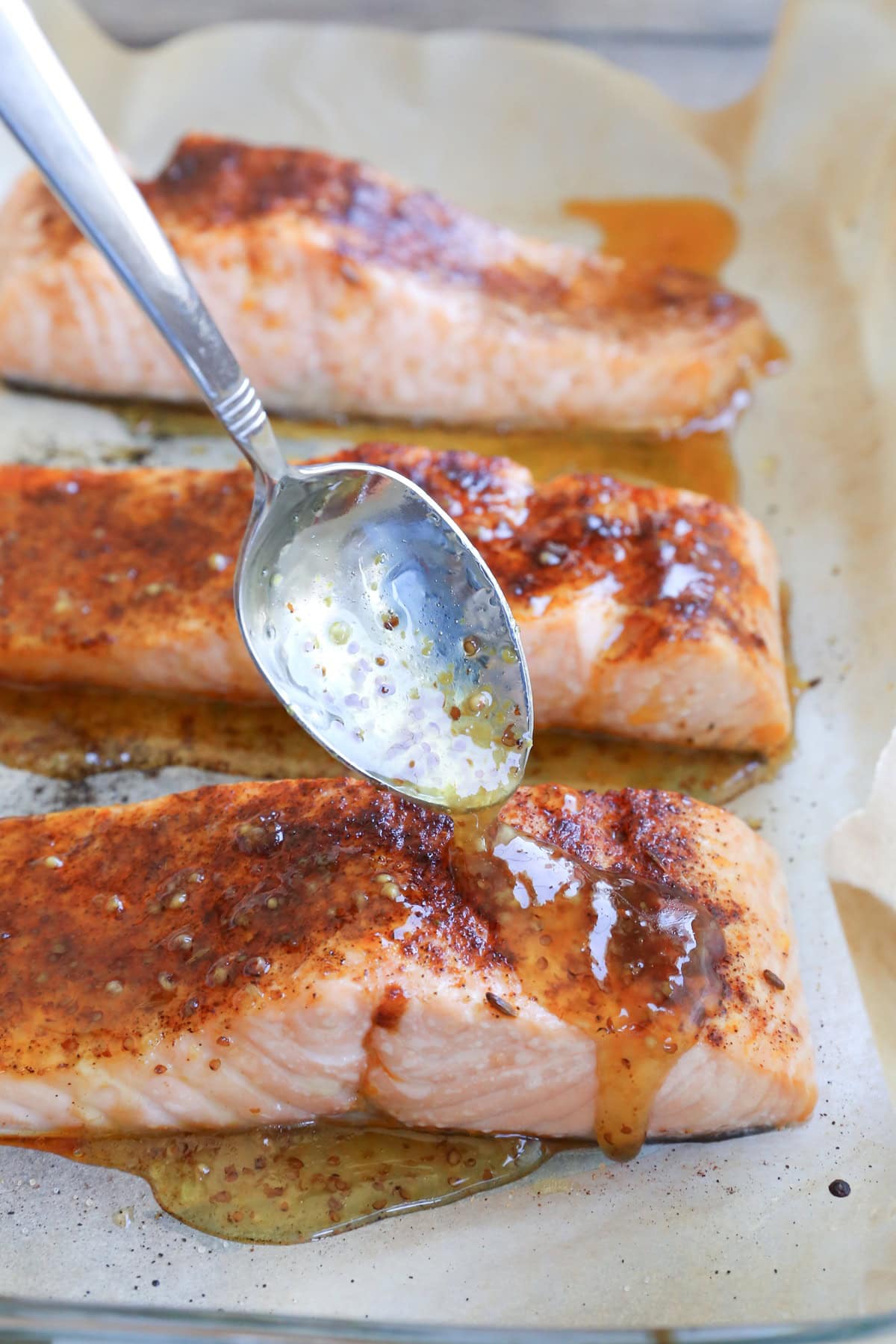 Spoon drizzling honey mustard sauce over cooked salmon