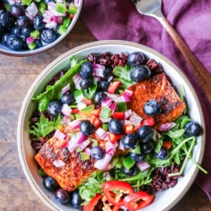 Bowl of crispy salmon on a bed of salad with blueberry salsa on top.