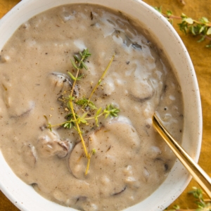 Dairy-Free Cream of Mushroom Soup in a oval ceramic bowl with fresh thyme sprinkled on top and a golden spoon to the side.