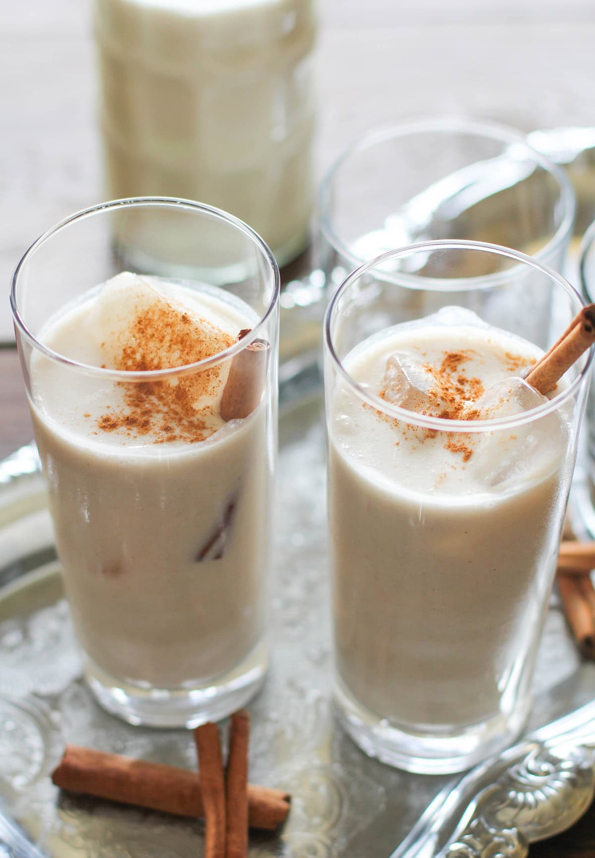 Two glasses of horchata with ice cubes and cinnamon sticks inside, sprinkled with cinnamon on top. Ready to drink.
