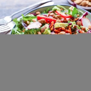 Big bowl of salad with fresh vegetables, almonds, avocado and lemon-parsley dressing. A purple napkin and fresh parsley to the side.
