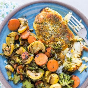 Easy Baked Cod Recipe with turmeric and paprika on a blue plate with roasted vegetables.