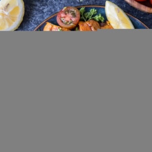 Plate of chicken shawarma with sauce and fresh vegetables to the side.