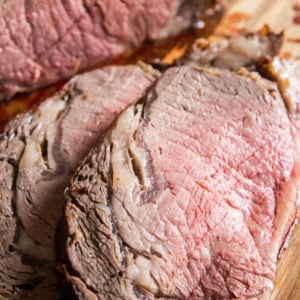 Prime rib cut into individual slices on a wooden cutting board with juices flowing out.