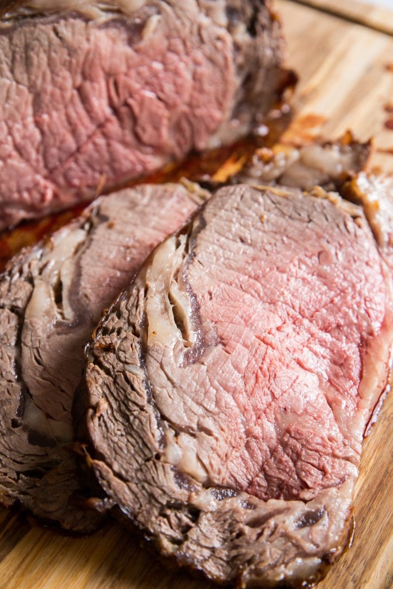 Prime rib cut into individual slices on a wooden cutting board with juices flowing out.