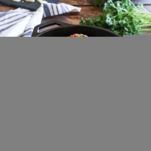 Cast iron skillet on a wooden table with a napkin and fresh parsley