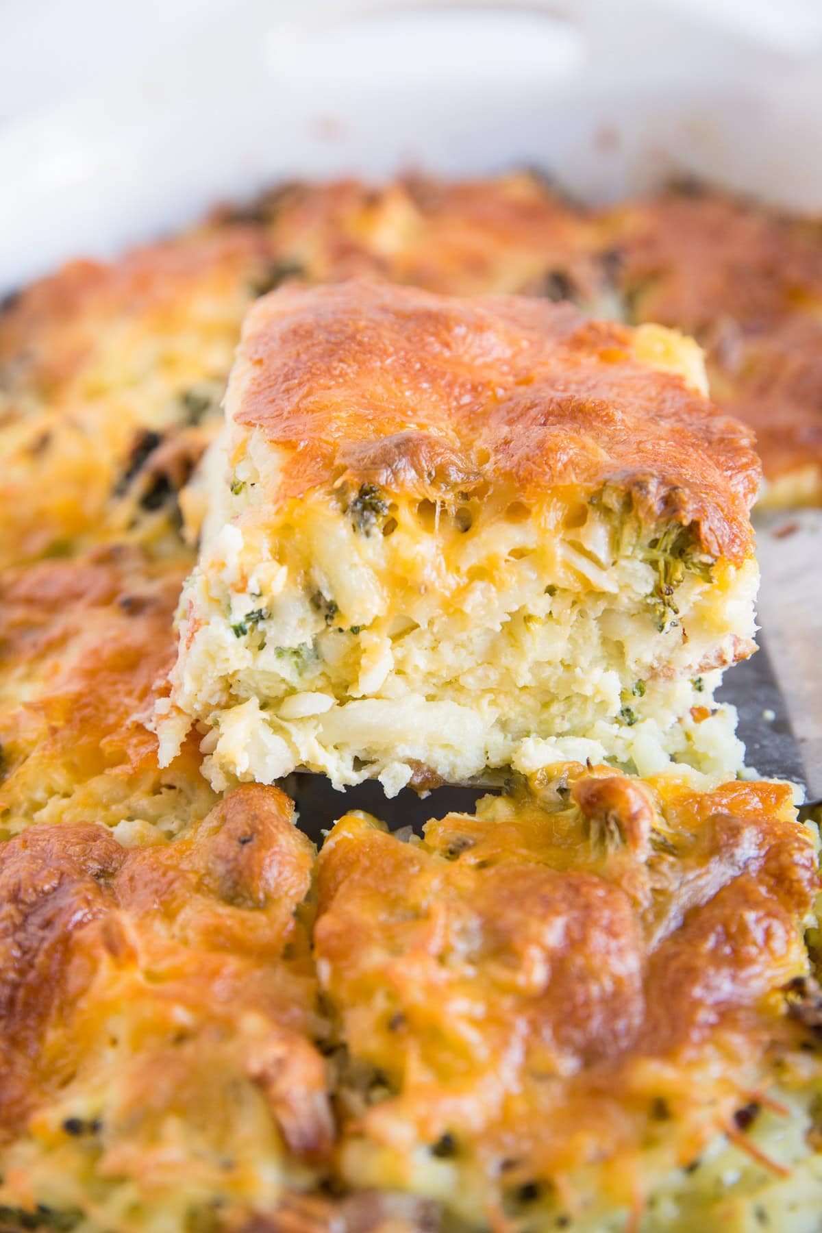 Spatula pulling a slice of broccoli cheddar egg hashbrown casserole out of a casserole dish.
