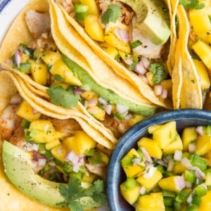 Easy Fish Tacos with Mango Salsa on a blue rimmed plate with a small bowl of mango salsa to the side. Ready to serve!