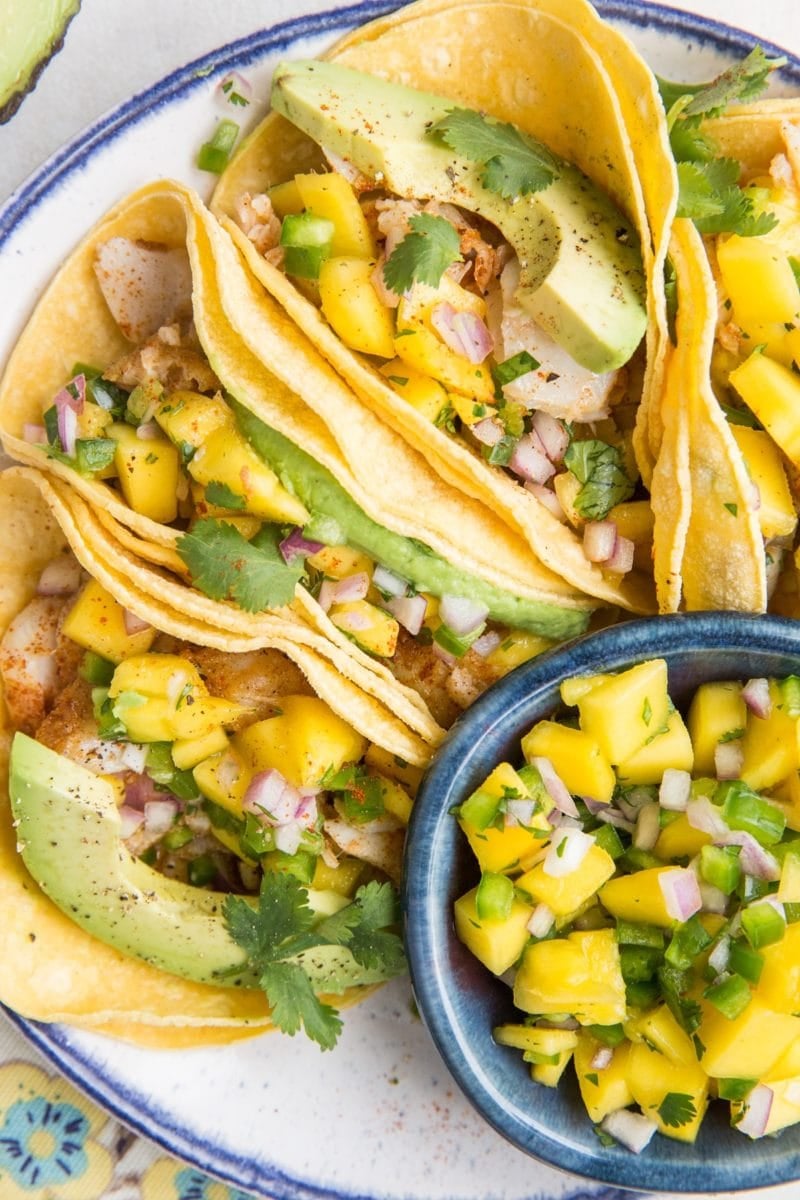 Easy Fish Tacos with Mango Salsa on a blue rimmed plate with a small bowl of mango salsa to the side. Ready to serve!