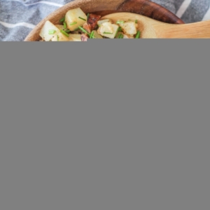 Large wooden bowl full of German potato salad with caramelized onions on top, ready to be mixed in.