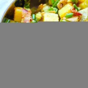 Large stainless steel bowl full of German Sweet Potato salad with bacon and green onions.
