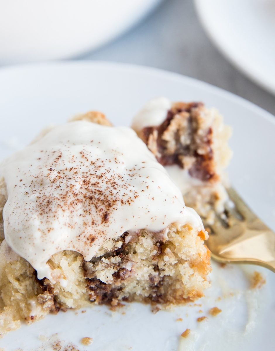 Large cinnamon roll with frosting on top with a bite taken out to see the cinnamon swirls on the inside.