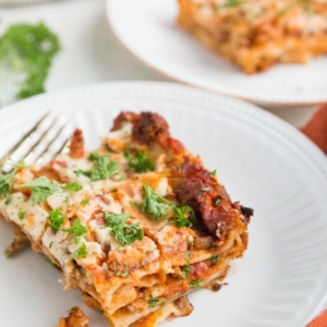 Two white plates with slices of lasagna on top and a red napkin to the side, ready to serve.