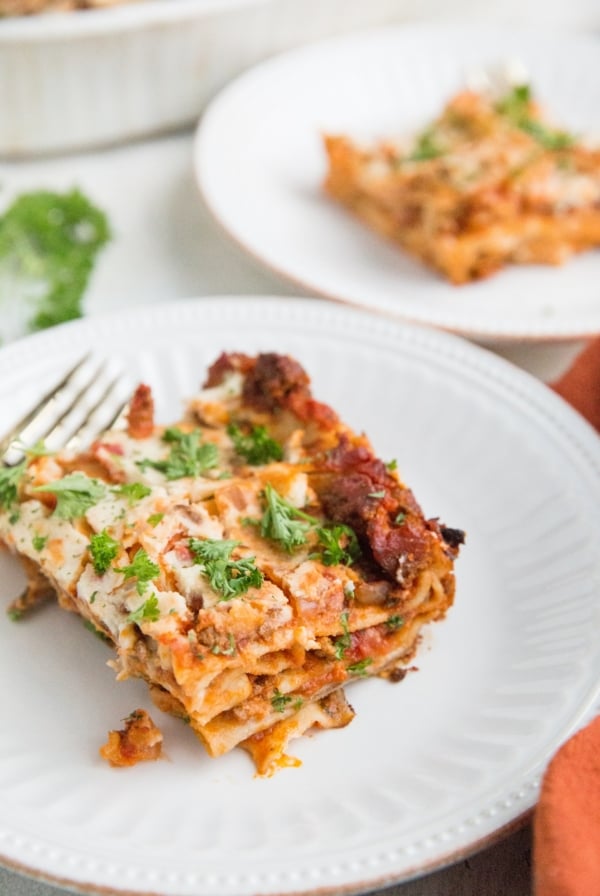 Two white plates with slices of lasagna on top and a red napkin to the side, ready to serve.