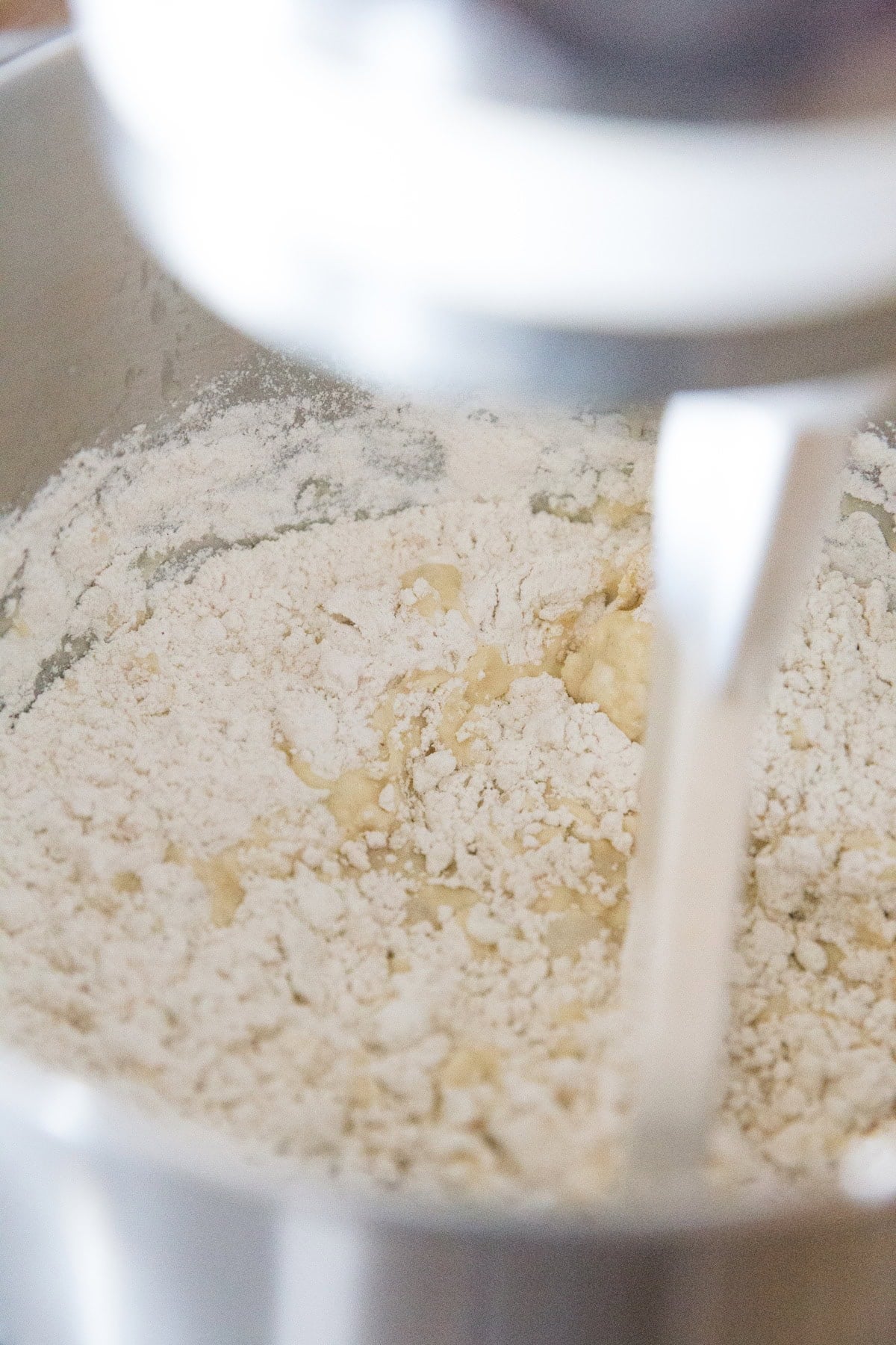 Stand mixer mixing in the eggs and flour with a paddle attachment.