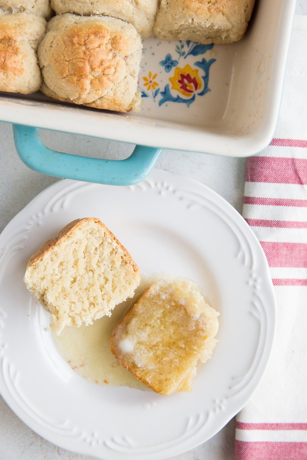 Hawaiian Roll cut in half on a plate with honey and melted butter on it with the dish of the rest of the rolls to the side.