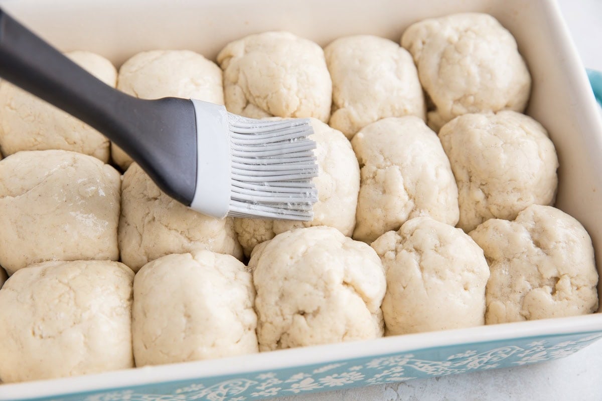 Brushing the egg wash onto the balls of dough using a silicone brush.
