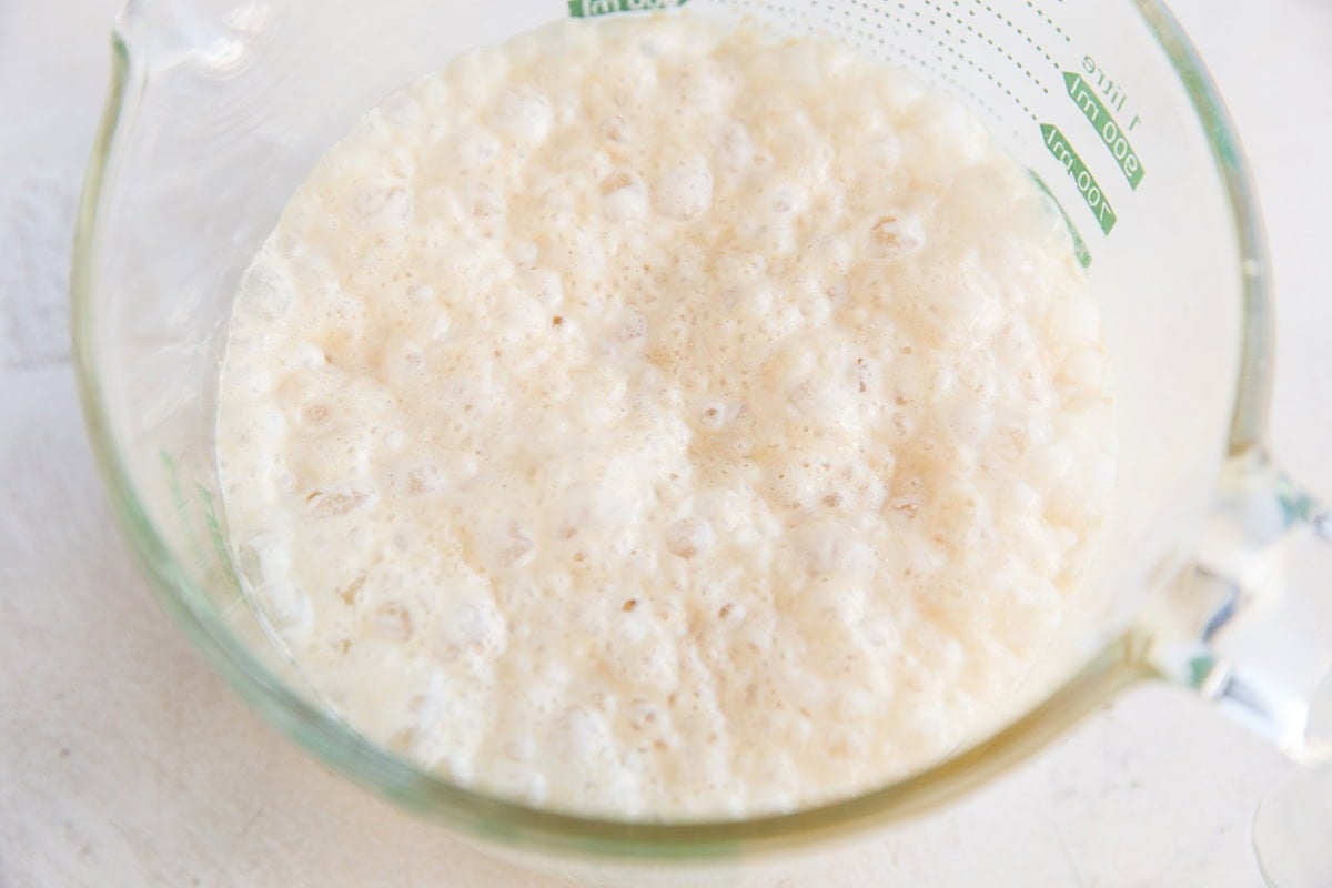 Activating the yeast in the coconut milk, pineapple juice and honey. A frothy bubbly mixture is pictured inside of a glass measuring cup.