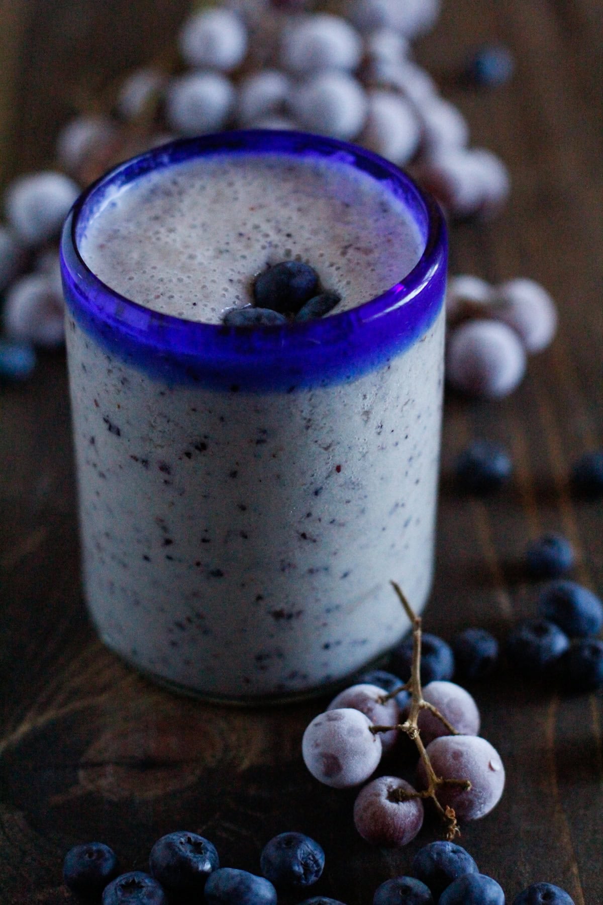 Grape and Blueberry Protein Smoothie with a secret protein ingredient, fresh grapes and blueberries next to the glass of smoothie.