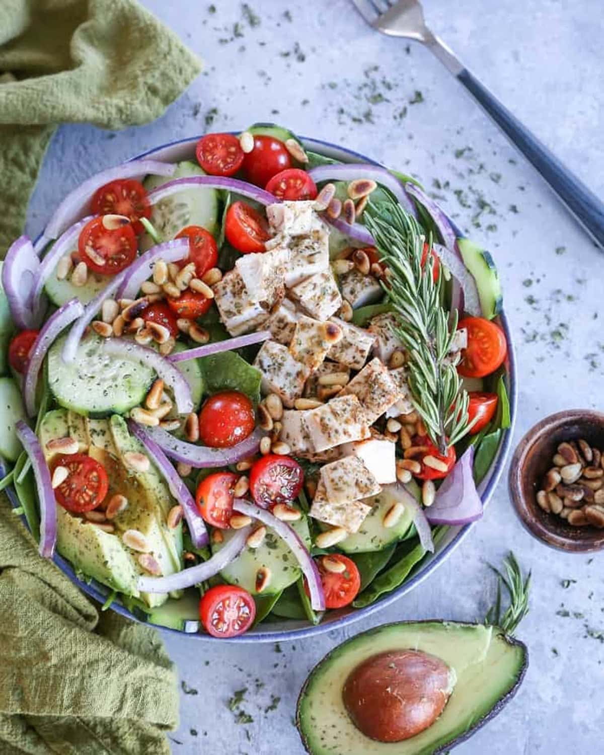 Herby Greek Spinach Salad in a large bowl with fresh avocado and dried herbs to the side.