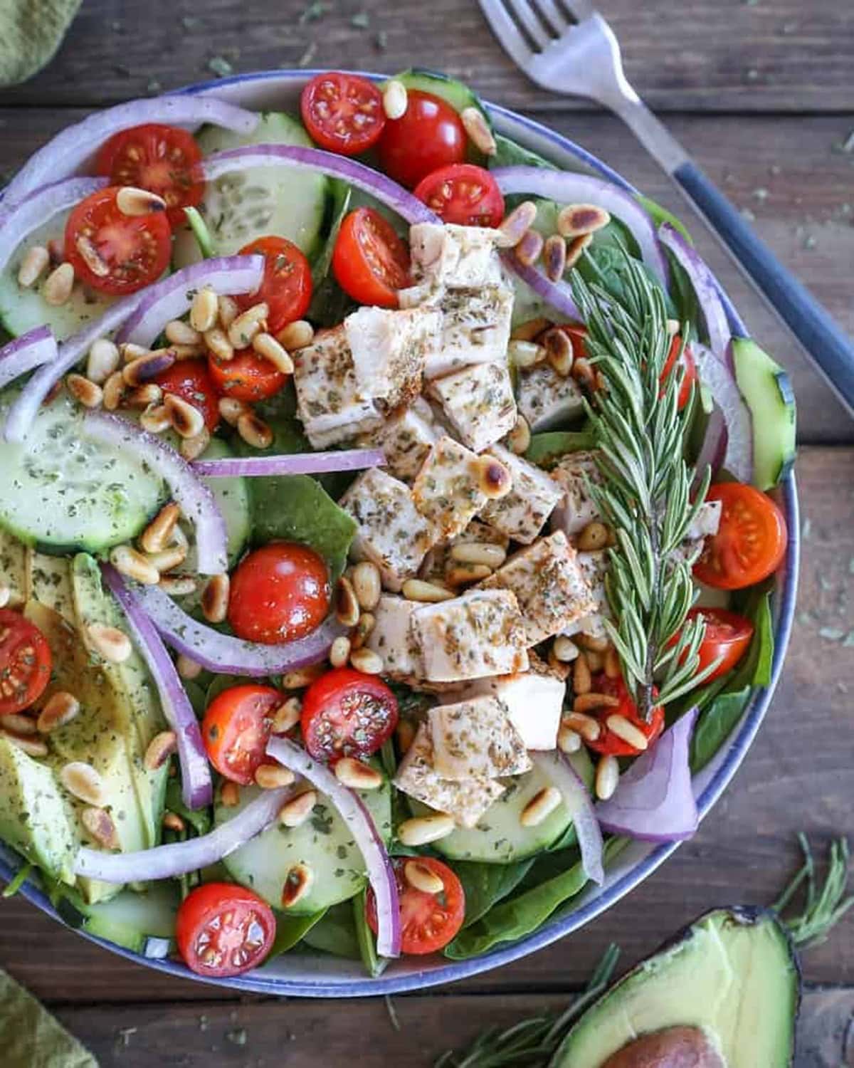 Large bowl of Greek spinach salad with chicken and fresh vegetables.