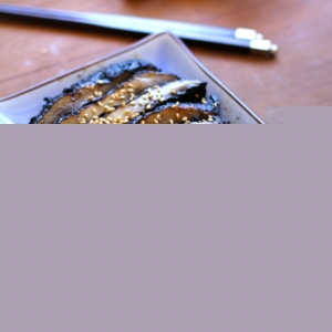 Grilled portobello mushroom cut into slices on a long blue plate with chopsticks and fresh ginger in the background, ready to serve as an appetizer.