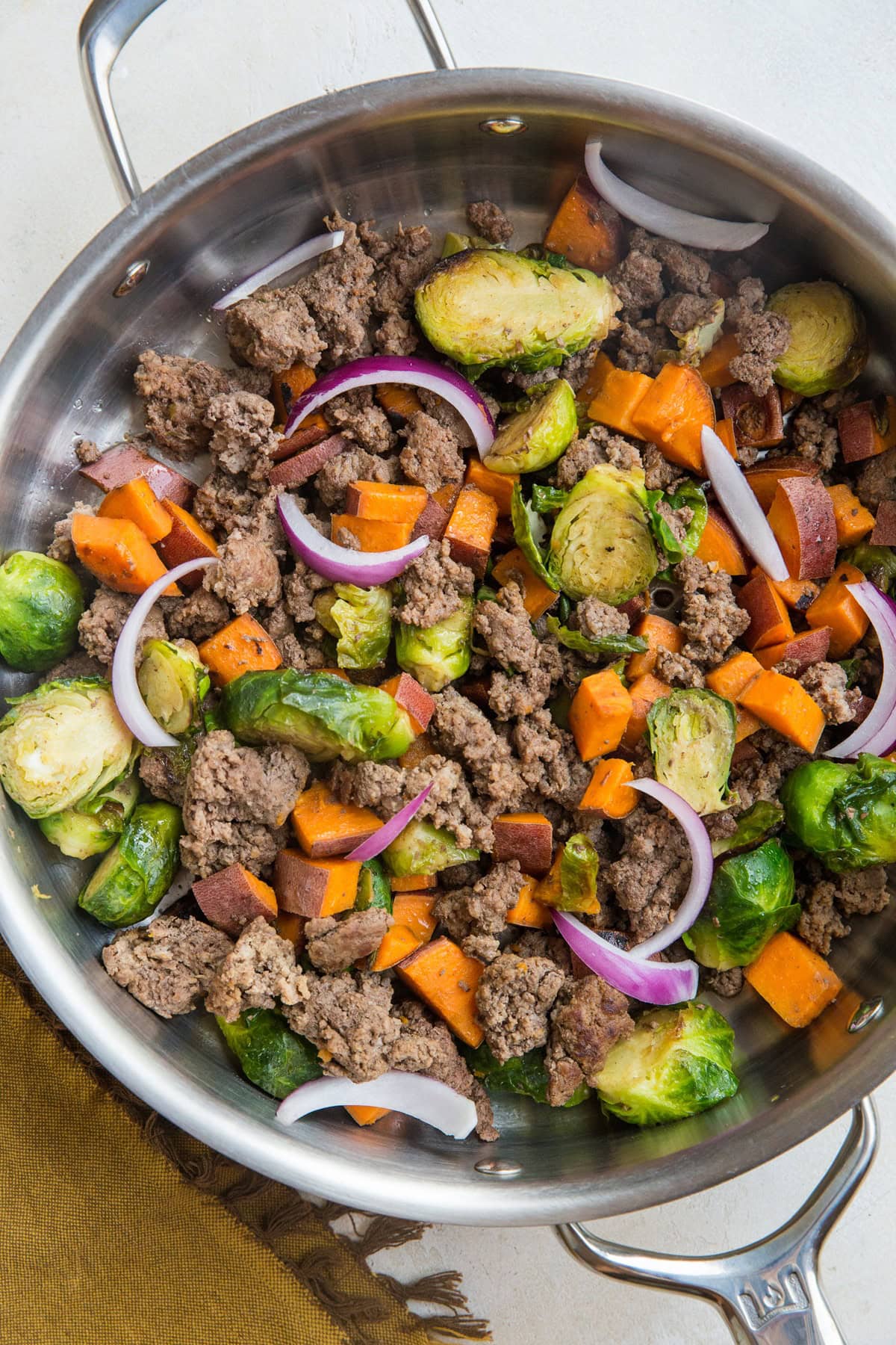 Stainless steel skillet full of ground beef, sweet potatoes, and brussel sprouts. Ready to eat.