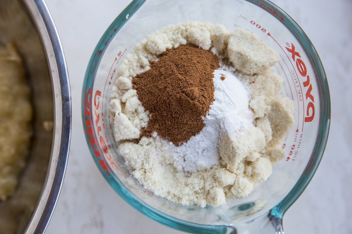 Ingredients for healthy apple muffins - a large measuring cup with all of the dry ingredients inside, ready to mix, and a bowl of wet ingredients to the side.