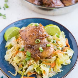 Filipino Chicken Adobo on top of sauteed cabbage on a blue plate with fresh limes to the side.