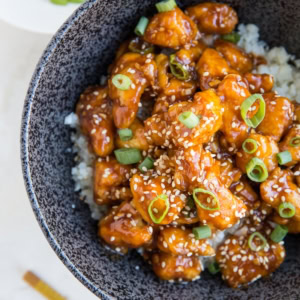 Large bowl full of rice and saucy general chicken sprinkled with sesame seeds and green onions. Ready to enjoy.