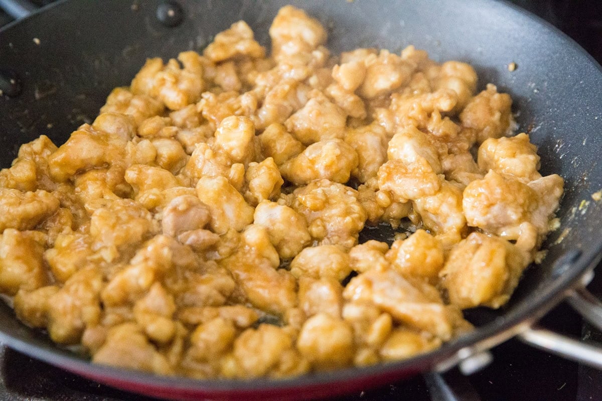 Orange chicken cooking in a skillet, almost finished.