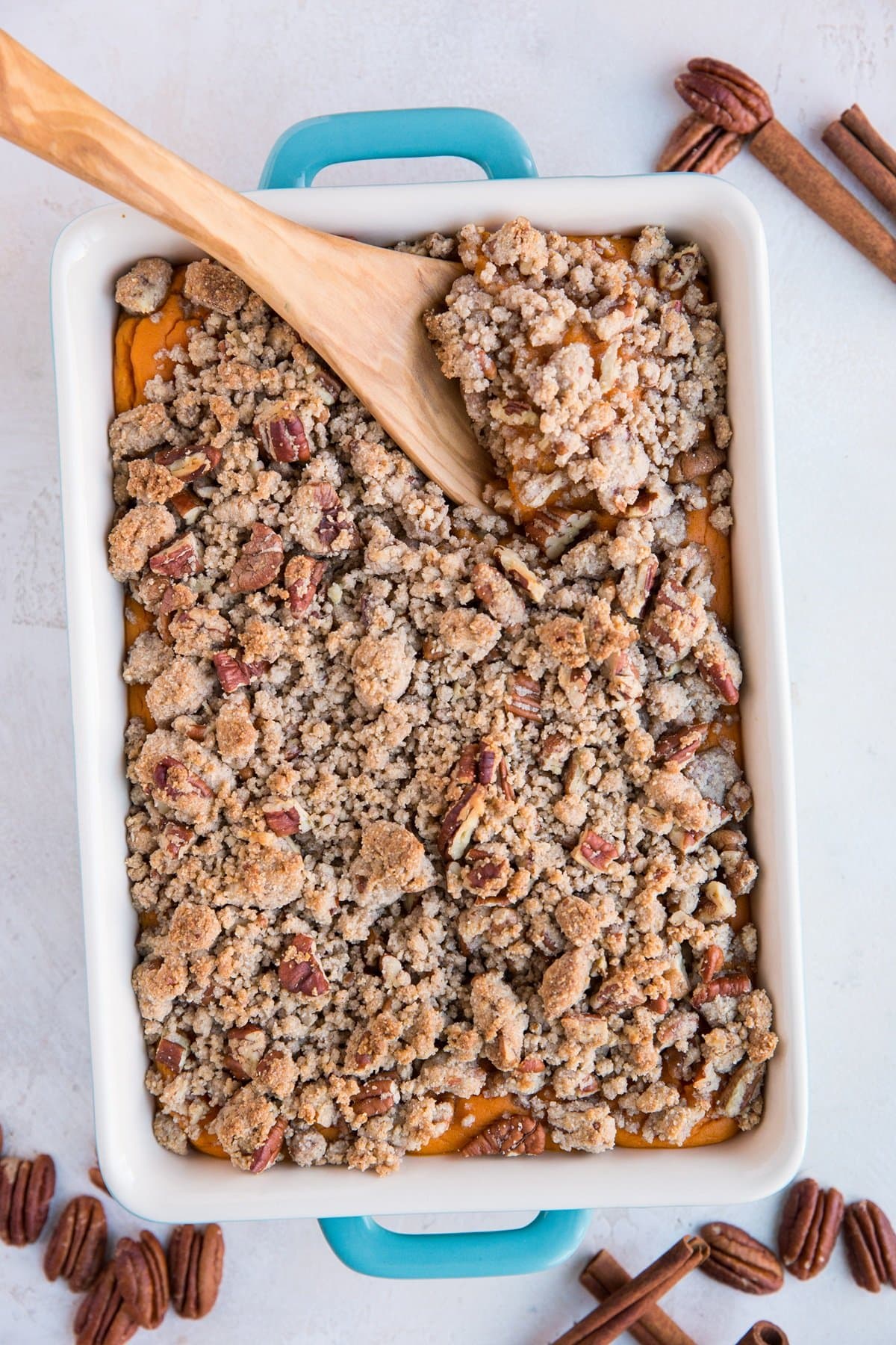 Casserole dish with blue handles full of Sweet Potato Casserole with pecans and cinnamon sticks all around. Ready to serve.