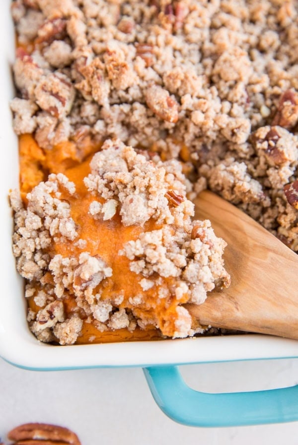 Blue casserole dish full of Sweet Potato Casserole with a wooden spoon scooping out some of the casserole.