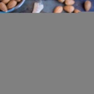 jar of homemade almond butter with a spoon inside of the jar and fresh almonds all around.
