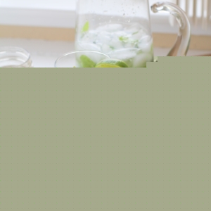 Two glasses of mint mojitos with a pitcher of mojitos in the background and fresh mint leaves to the side.