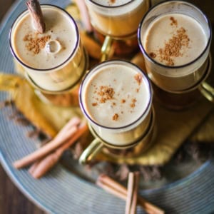 Four glasses of Hot Buttered Rum on a serving platter with cinnamon sticks around.